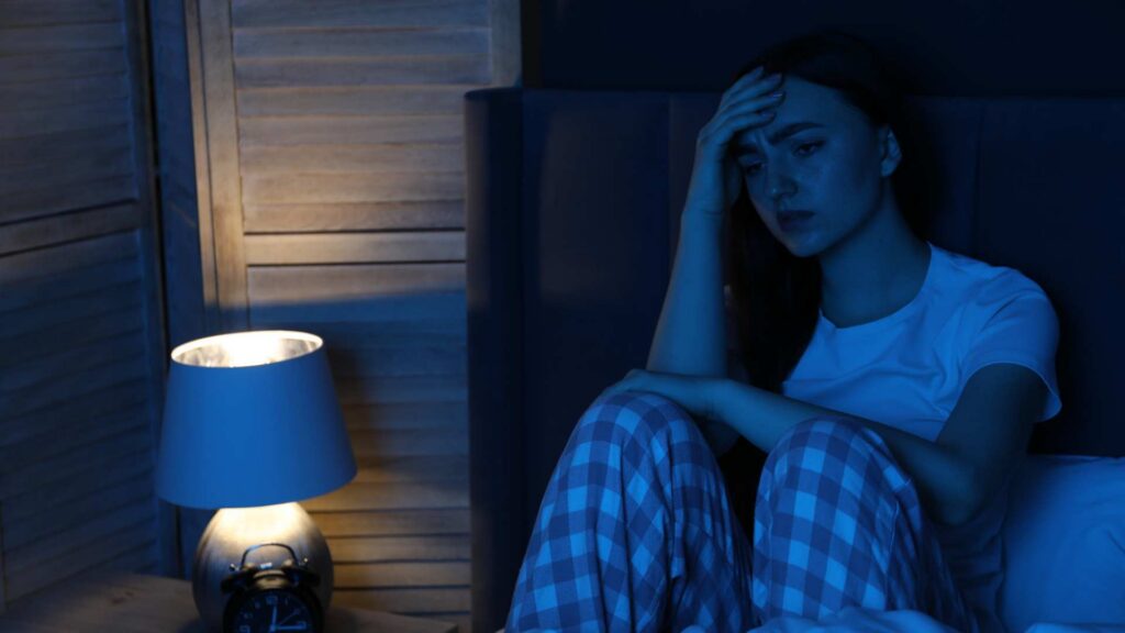 A person sitting awake in bed at night, showing trouble sleeping linked to alcohol withdrawal