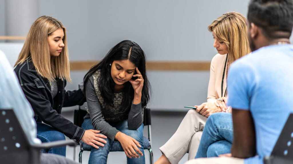 A small group sitting in a circle during a support session, showing different stages of care in addiction treatment