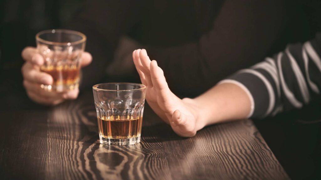 Close‑up of someone declining a drink, showing a stop gesture toward a glass of liquor