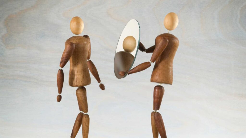 Personal inventory of addiction: a wooden figure holding up a mirror to another wooden figure, signifying self-reflection.
