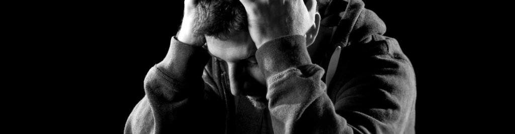 Grief and addiction: A black-and-white picture of a man holding his head in his hands.