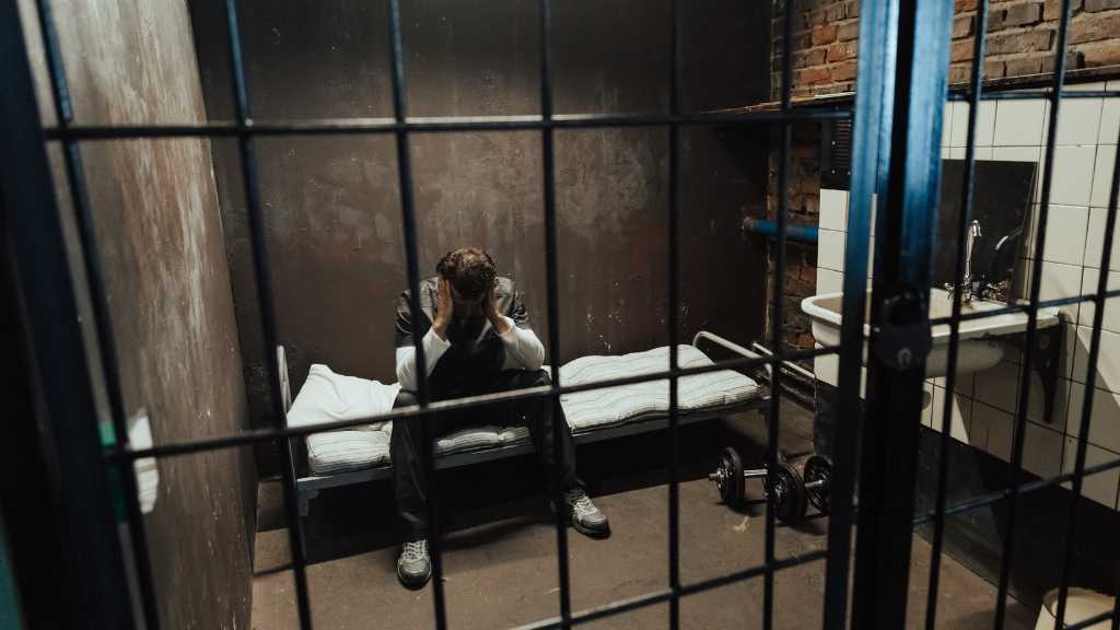Person sitting alone in a jail cell illustrating opioid addiction and incarceration and the impact of opioid withdrawal in jail.